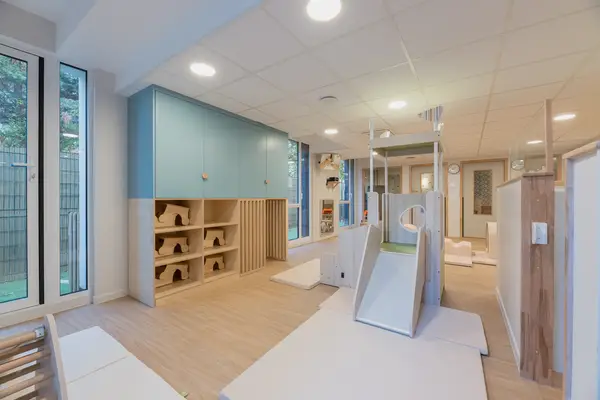 Salle de motricité de la crèche Les Bébés Explorateurs Cormeilles-en-Parisis (95240) – toboggan gris, étagères Montessori bois en arches, grandes armoires bleu canard, matelas blancs au sol, miroirs et baies vitrées sur jardin